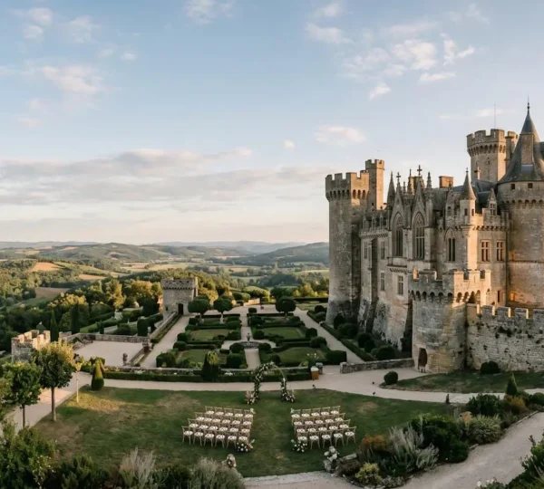 Majestic European castle with stone towers overlooking formal gardens, prepared for a large wedding celebration with elegant outdoor ceremony setup