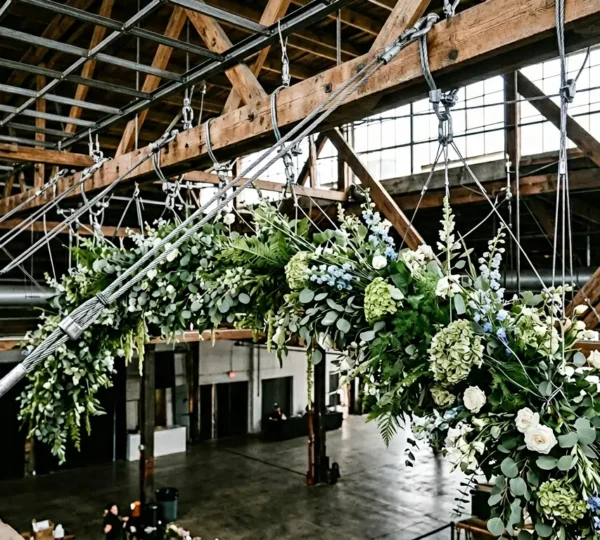 Professional overhead floral installation suspended from exposed beams showing engineering mechanics and structural rigging points