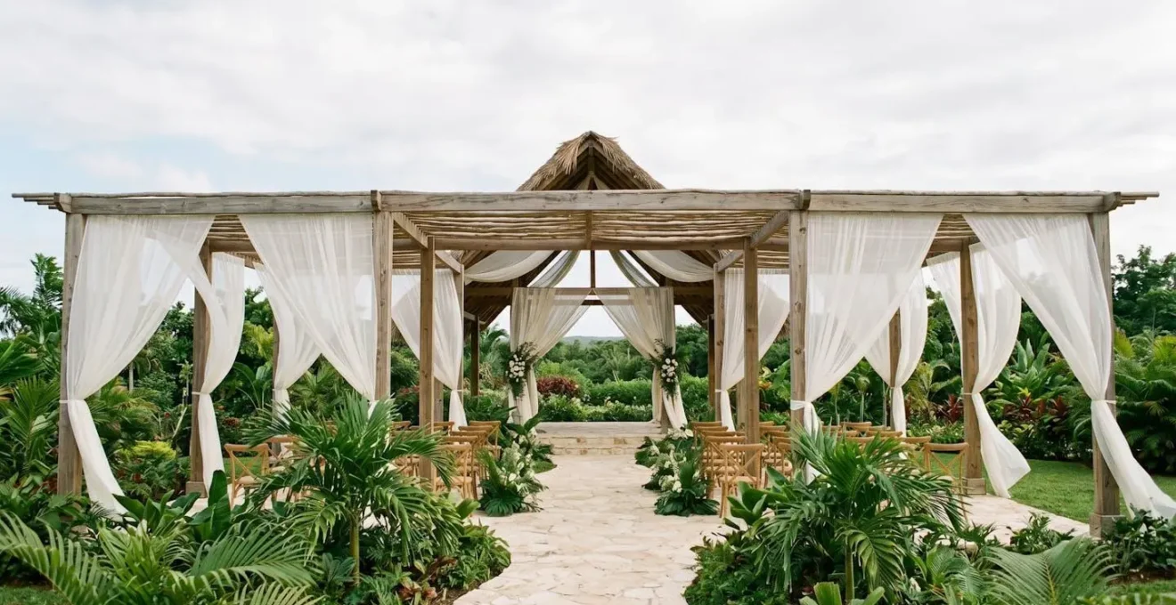 Wide shot of elegant open-air wedding pavilion with flowing white curtains and tropical greenery in natural light