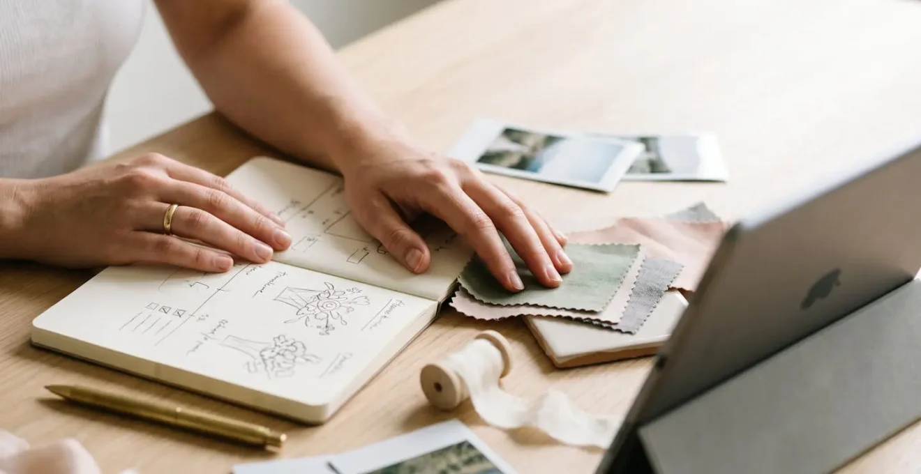Hands organizing wedding planning materials with both digital tablet and handwritten notes on marble surface