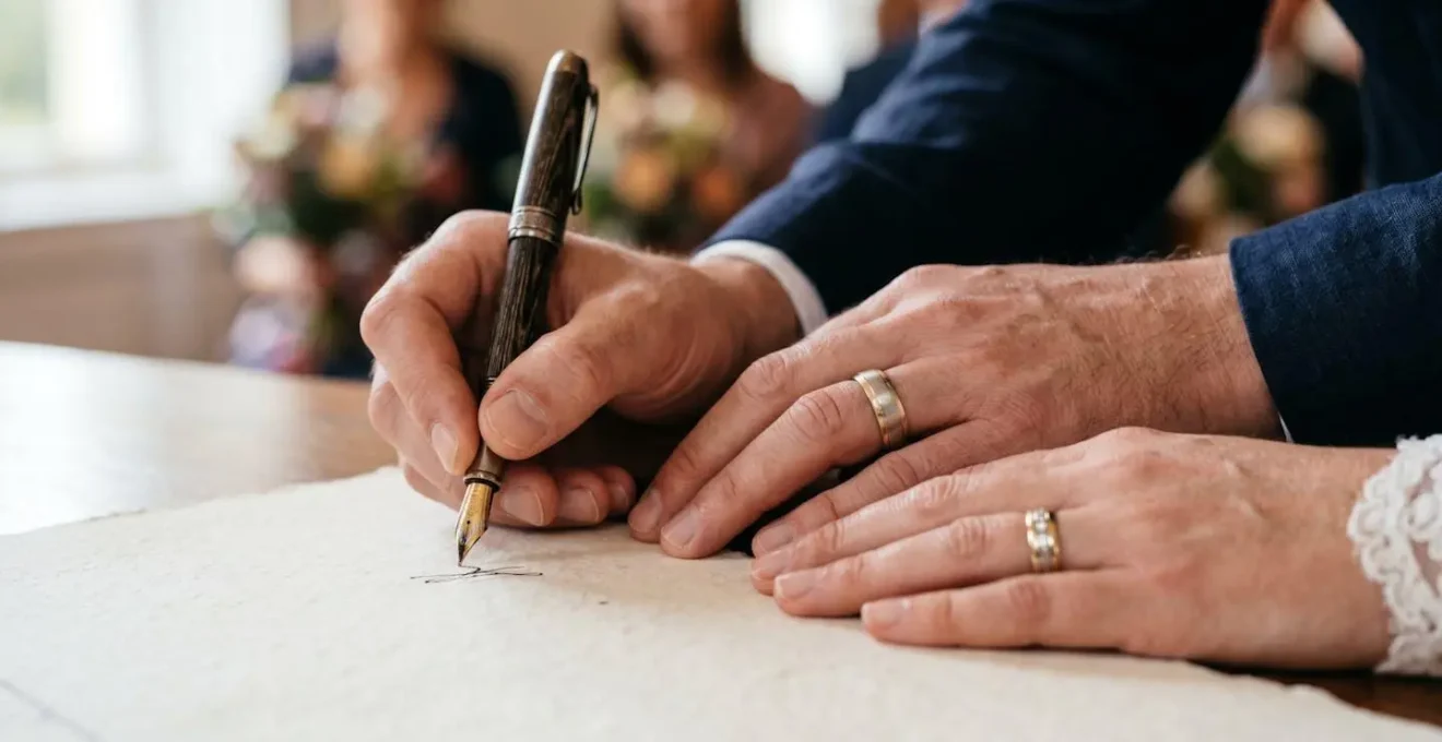 Close-up of hands signing official wedding documents with elegant wedding rings visible